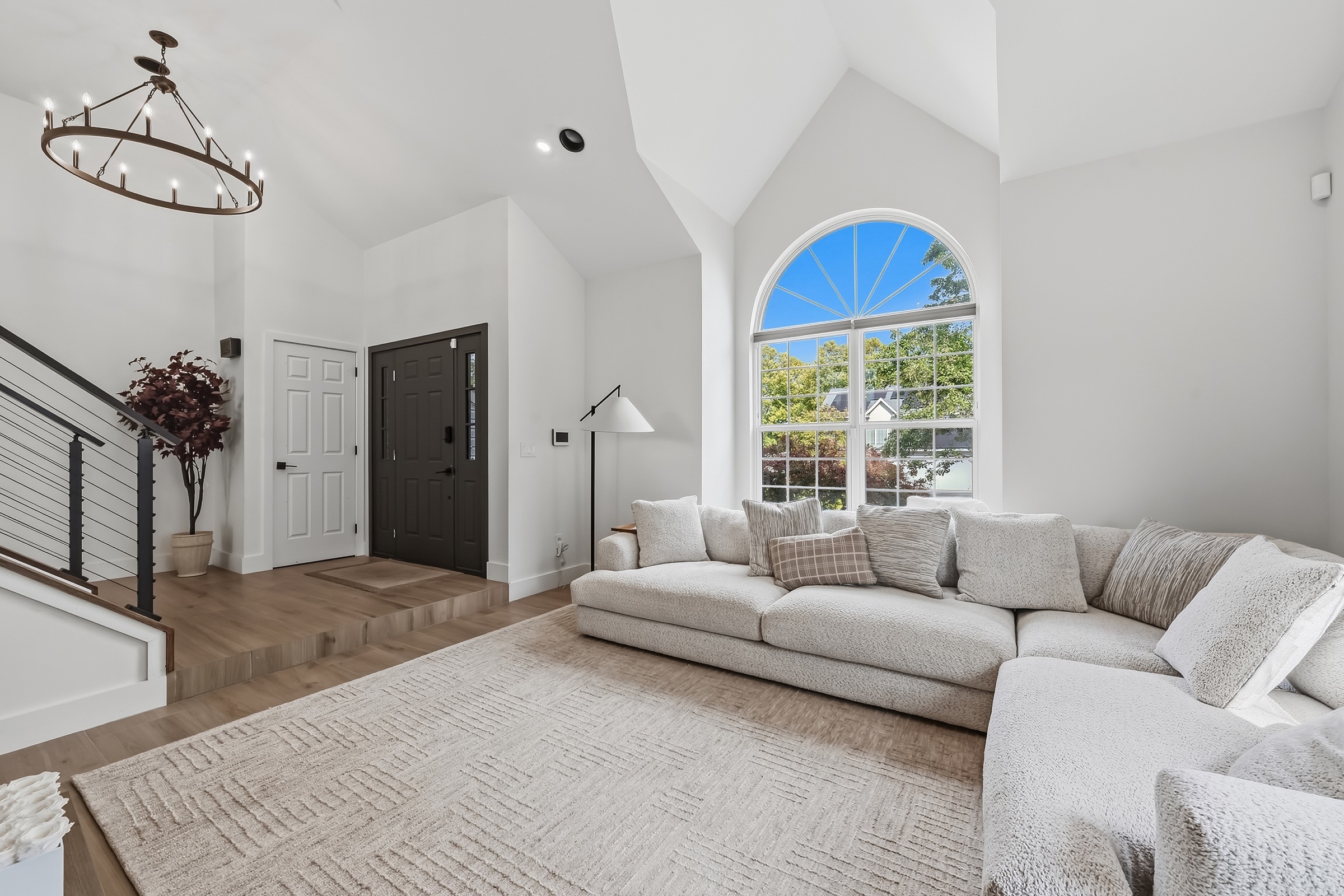 Bright modern living room with a dramatic arched window, staircase and layered natural light
